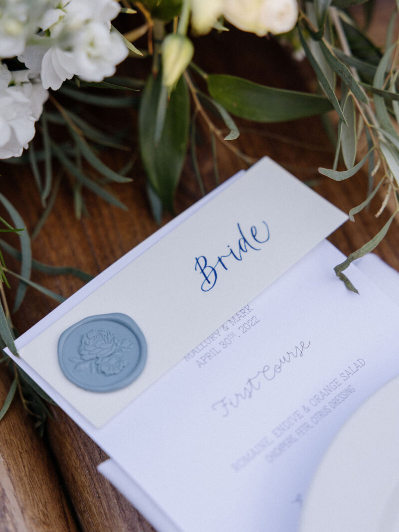 Calligraphy name cards with navy lettering and a dusty rose wax seal for an outdoor wedding