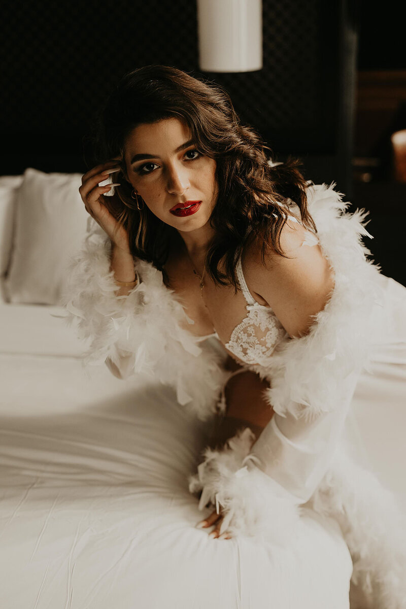 woman sitting on a bed in white lingerie and a feather robe