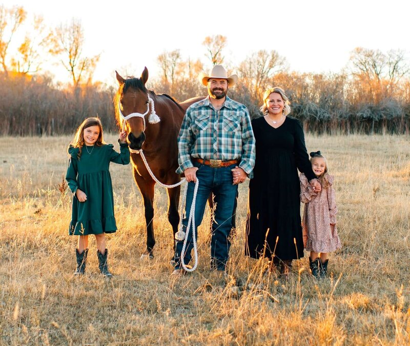 dustin hulme of elk ridge builders poses with his wife, two daughters and their horse