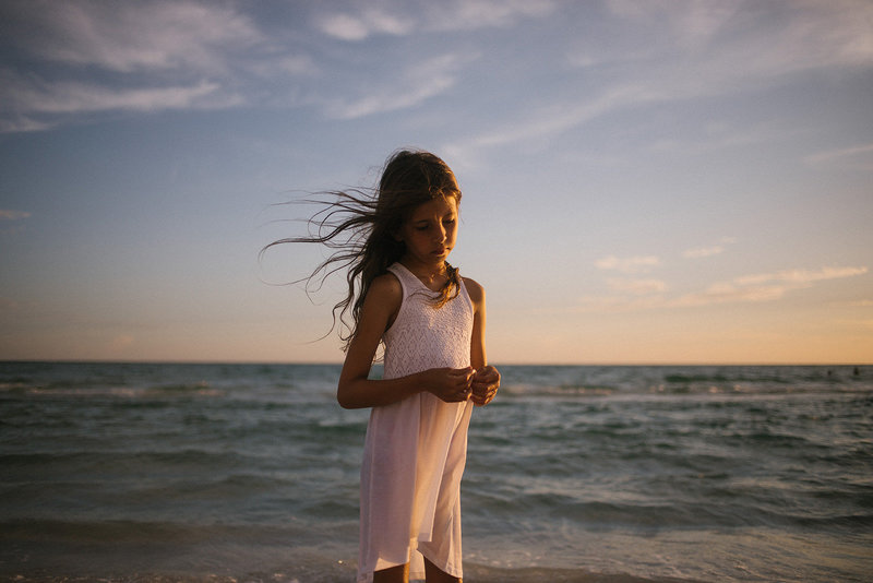 Little girl with long brown hair wearing  white dress on a beach in Siesta Key