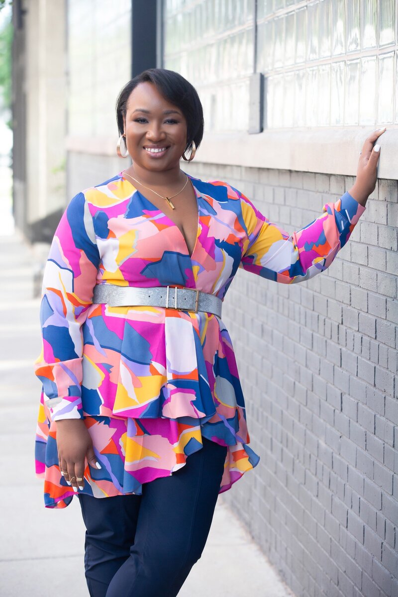 Shemiah Derrick smiling in colorful shirt standing in Chicago by gray brick wall.