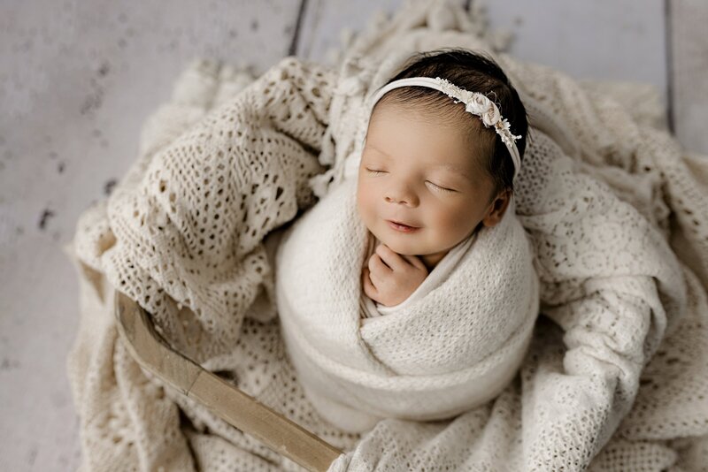 newborn baby girl is wrapped in cream in a basket during her waxhaw studio session
