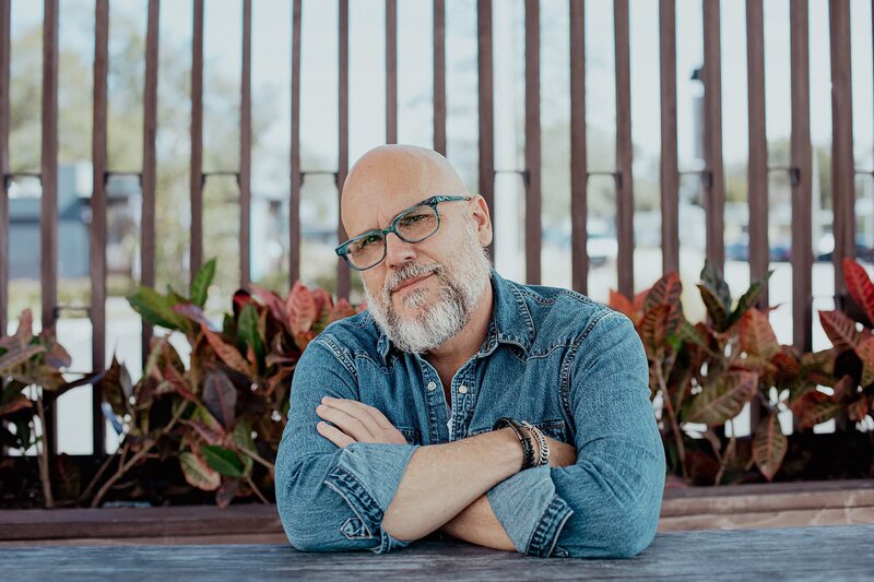 Sky wearing denim with teal glasses on, arms crossed smirking at camera