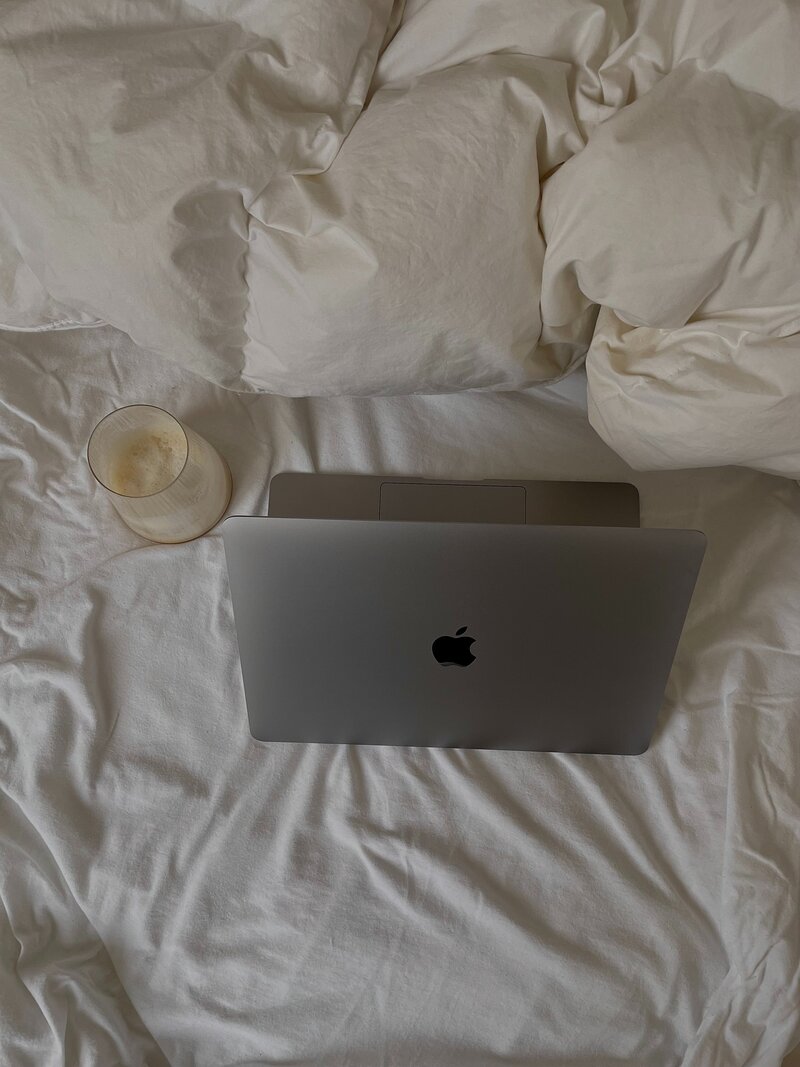 Macbook sitting on bed with with douvet with milky beverage beside.