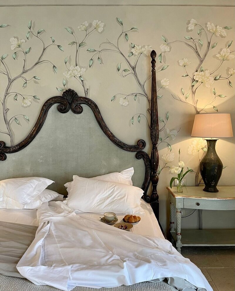 A four-poster canopy bed backdropped by a floral mural wallpaper