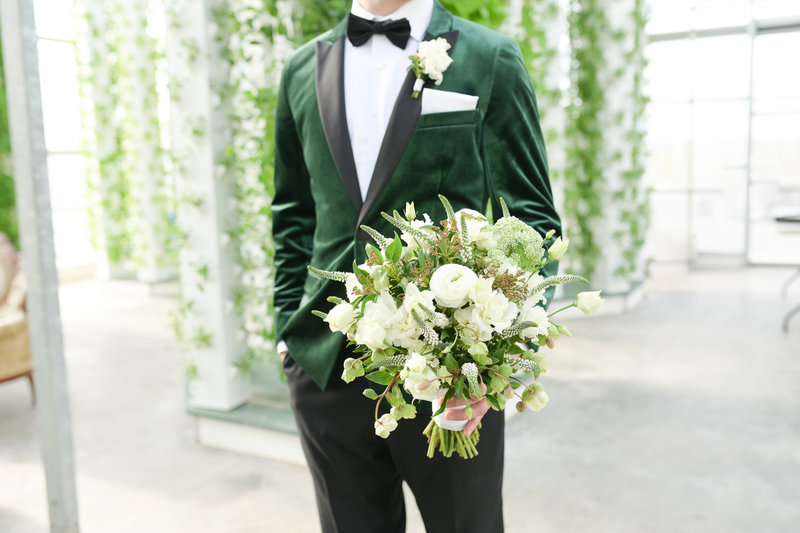 Groom in green velvet dinner jacket holds bouquet