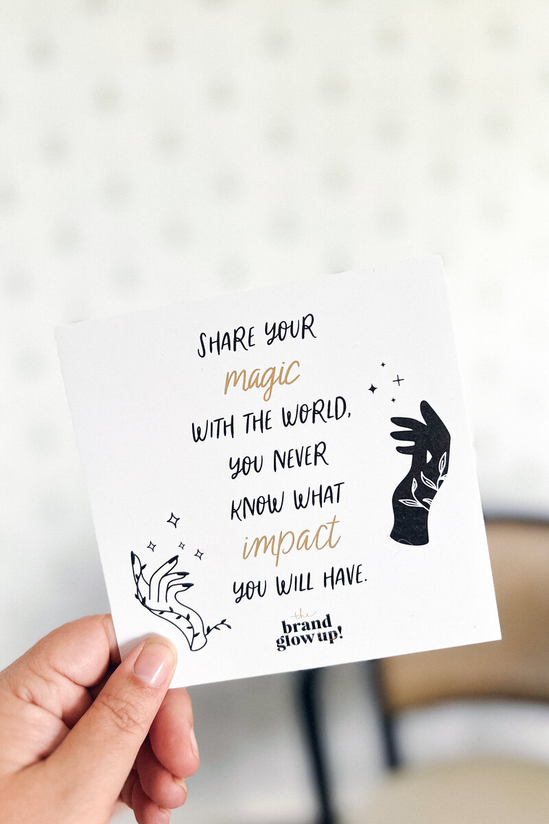 A hand holding a square art print that says "Share your magic with the world. You never know what impact you will have."