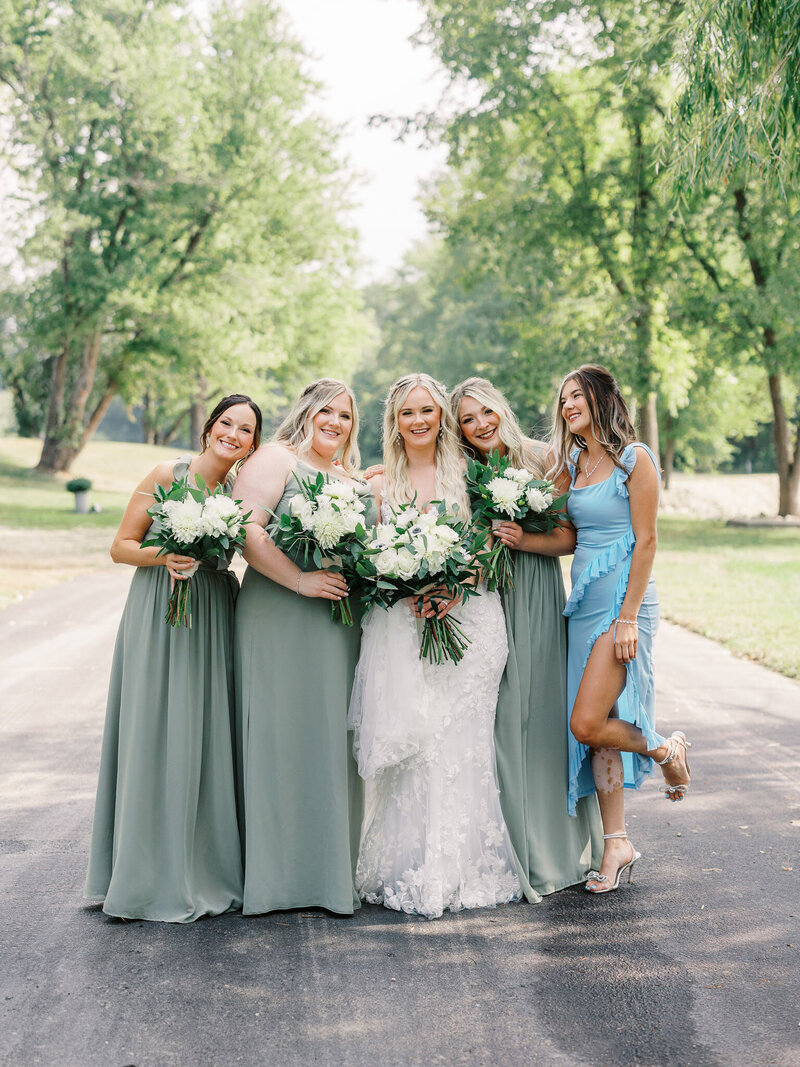 Bride and her bridesmaids standing close together and smiling with trees in the background