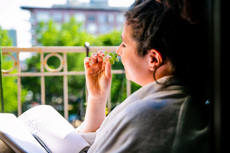 Woman smells the scent of her plant cutting while sitting on her apartment balcony