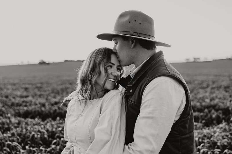 A groom kissing his partner’s forehead during an intimate elopement photoshoot in a rural location.