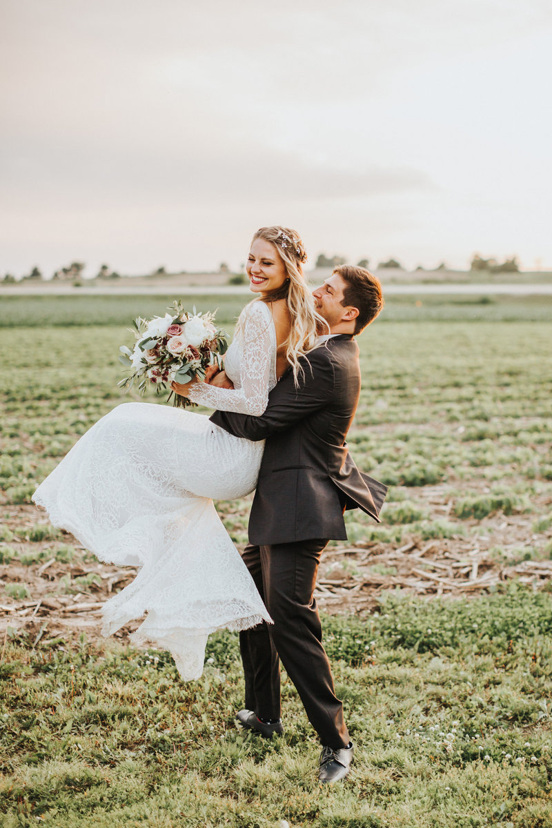 A cute, boho-styled couple hug and spin around iin an Iowa field at sunset on their wedding day.