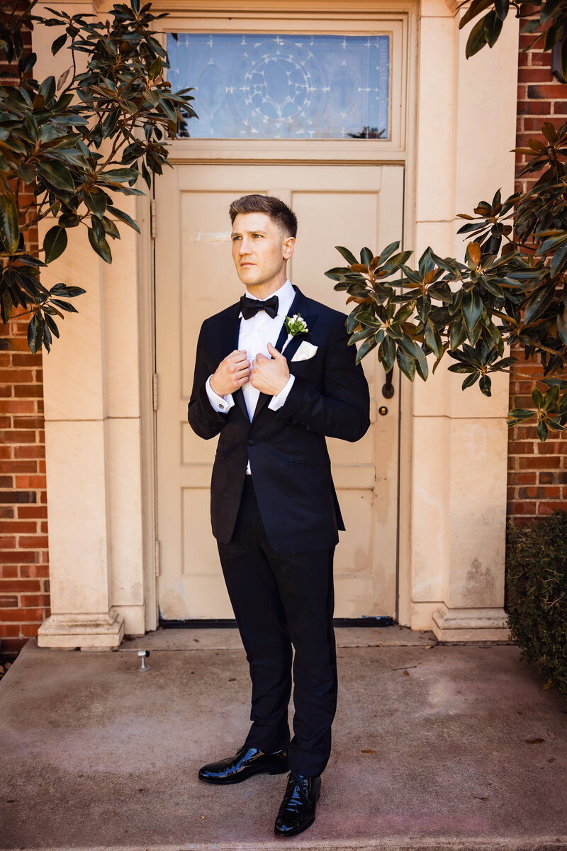 groom in tuxedo standing outside chapel near magnolia tree