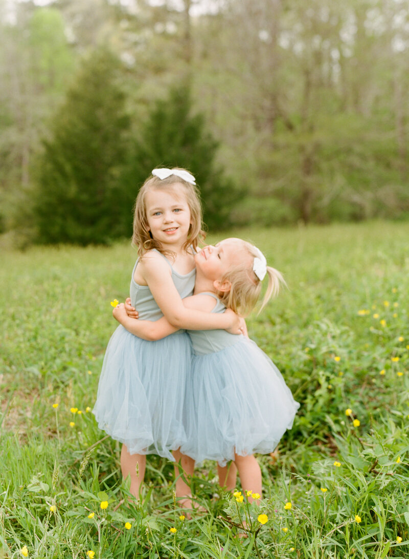 Sisters hugging in a field of flowers. Image by Raleigh family photographer A.J. Dunlap Photography.
