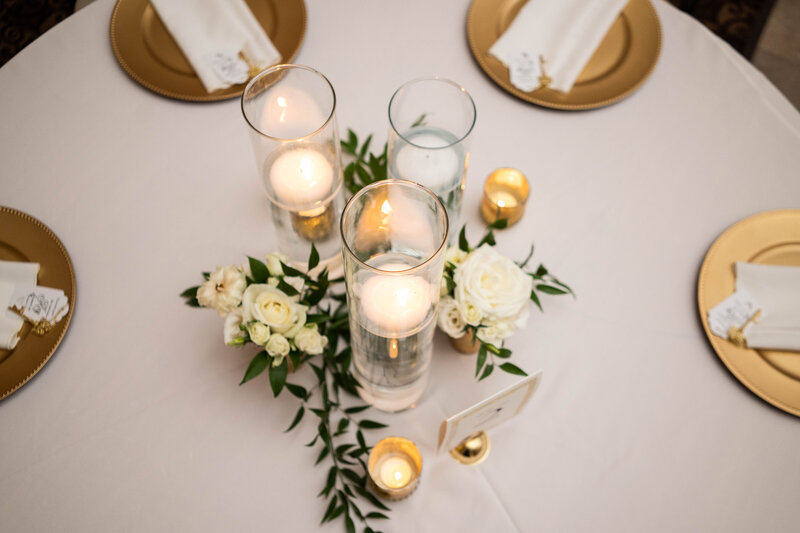 3 tea-light candles on a table with white roses and a table card