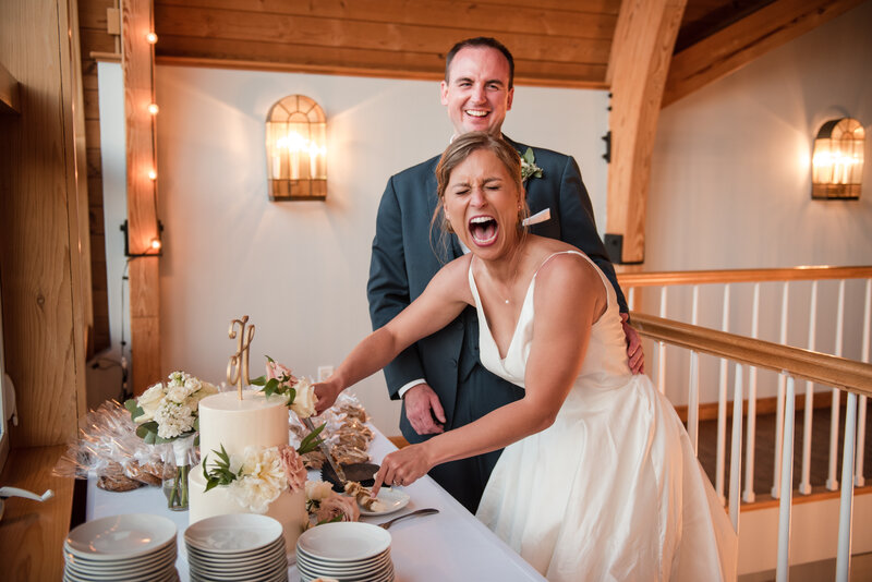 Bride cuts cake while laughing with groom standing behind her at a mystic yachting club wedding.
