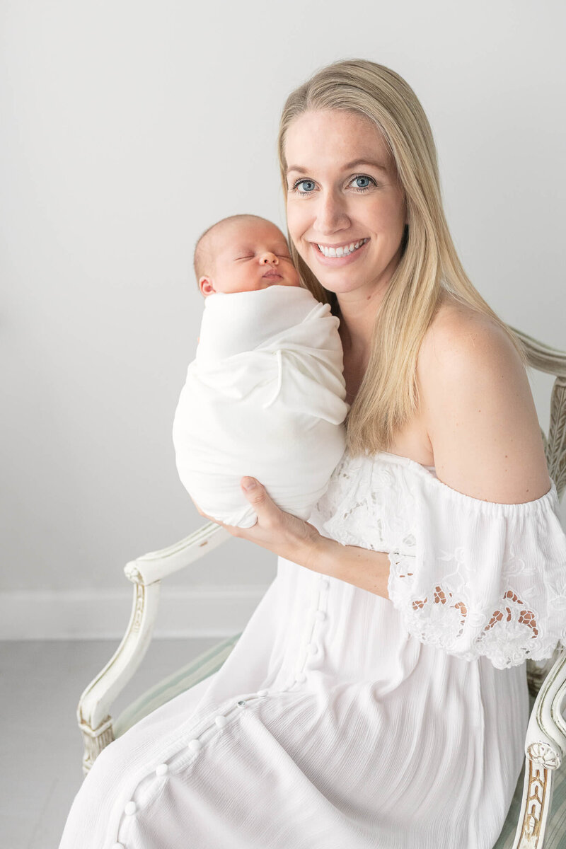 new mom in white smiles holding newborn boy