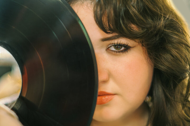Closeup portrait of a high school senior girl covering her face with a record