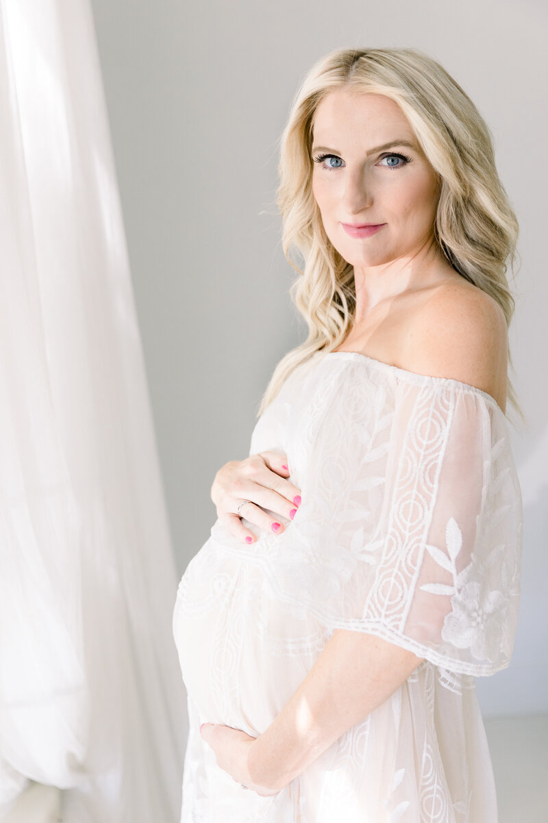 Expecting mother in studio in ivory lace dress holding baby bump taken by maternity photographer sacramento kelsey krall