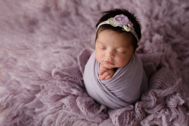 baby girl wrapped in lavender swaddle and posed on a purple rug