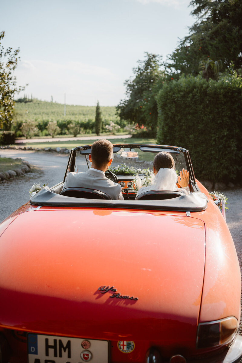 Groom and bride leaving the ceremony on an old red car in an Italian wedding close by Verona, at Antica Dimora del Turco