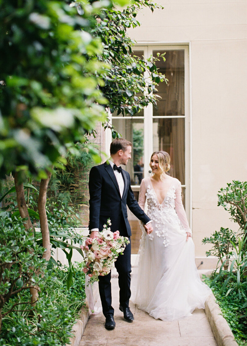 bride and groom walking holding hands in the orangery, groom holding large pink blush colour bouquet