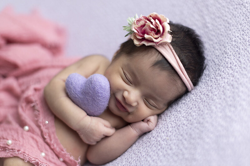 Newborn girl hugging purple heart.