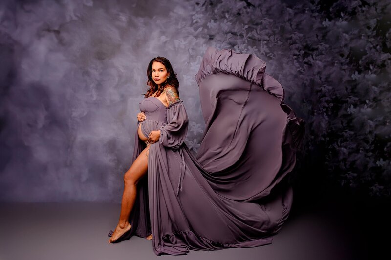 Pregnant mother in a Dusty purple dress that's flowing in a studio session on a purple background