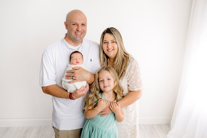 father holds his newborn son as his wife and daughter stand beside them