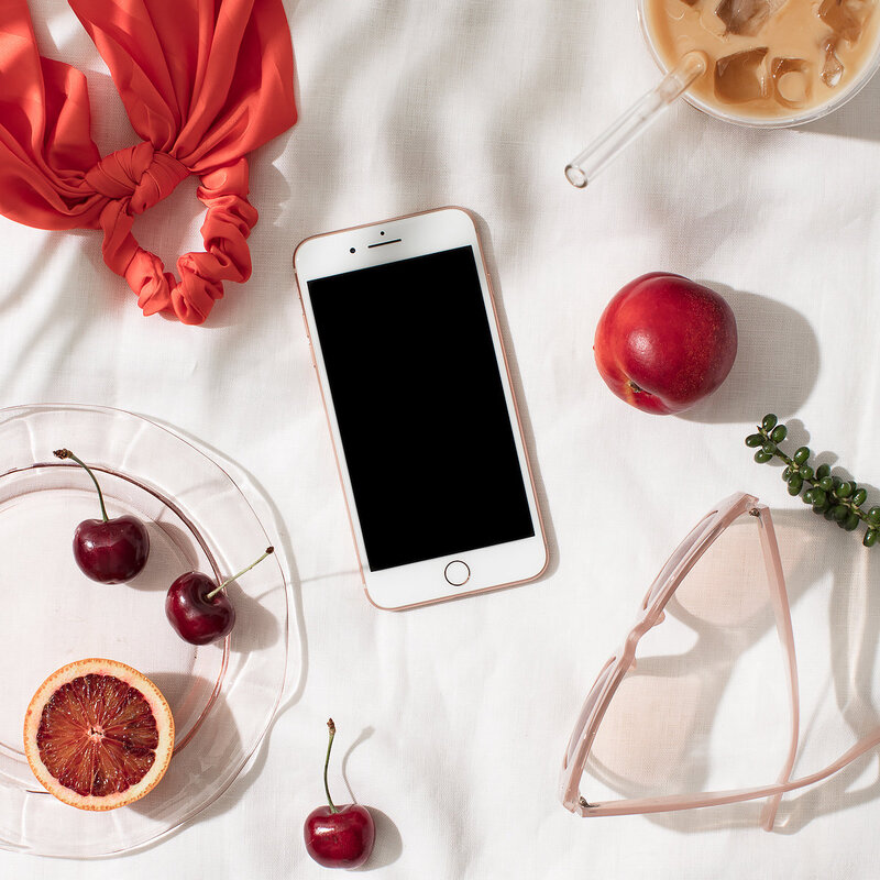 A photo of a hair band, a cup of coffee, a cell phone, an apple, a plate with cherries and an orange, and a pair of sunglasses