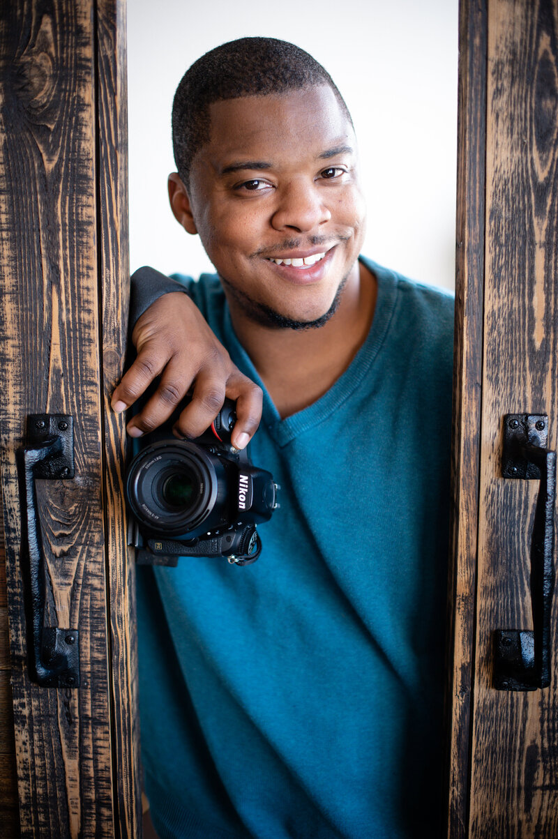 Michael T Davis, a wedding photographer in ATX, smiles at the camera while holding a Nikon camera