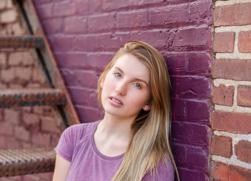 close up of high school senior girl leaning against purple brick backdrop