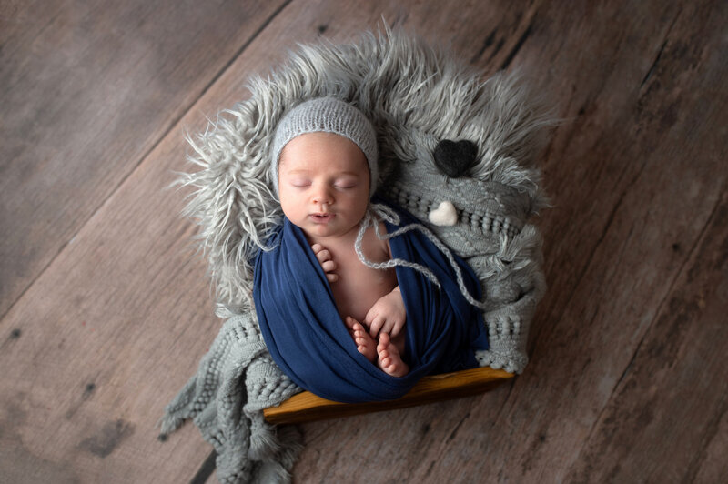 Newborn baby boy swaddled in wooden box during newborn studio session.