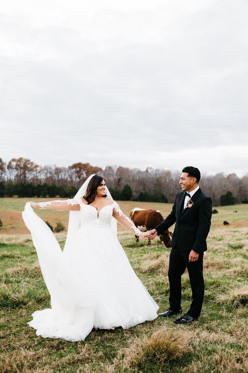 bride dancing in a field full of horses as her groom holds her hand and smiles at her for a winter wedding