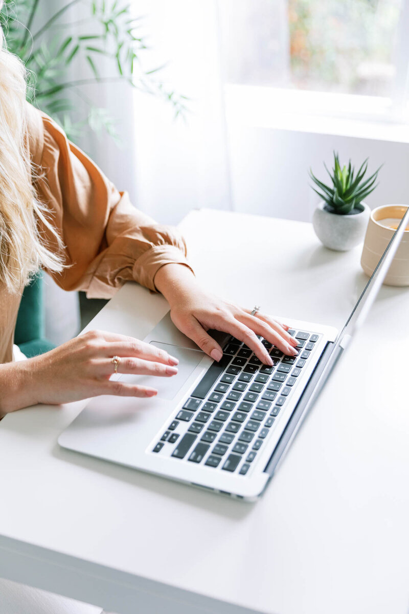 woman typing on computer with window and tree in the background