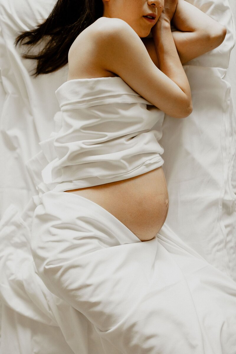 Pregnant person standing with hands resting on bare belly, wearing a cozy sweater