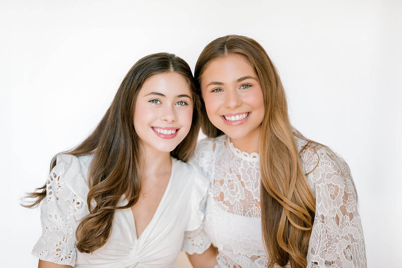 Twin senior girls from St. Joseph's Academy smile during a studio session dressed in all white.