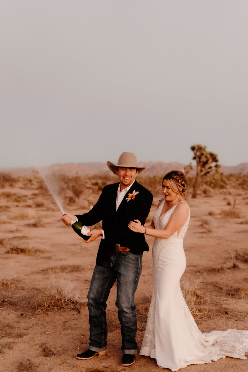 bride and groom pop champagne in desert