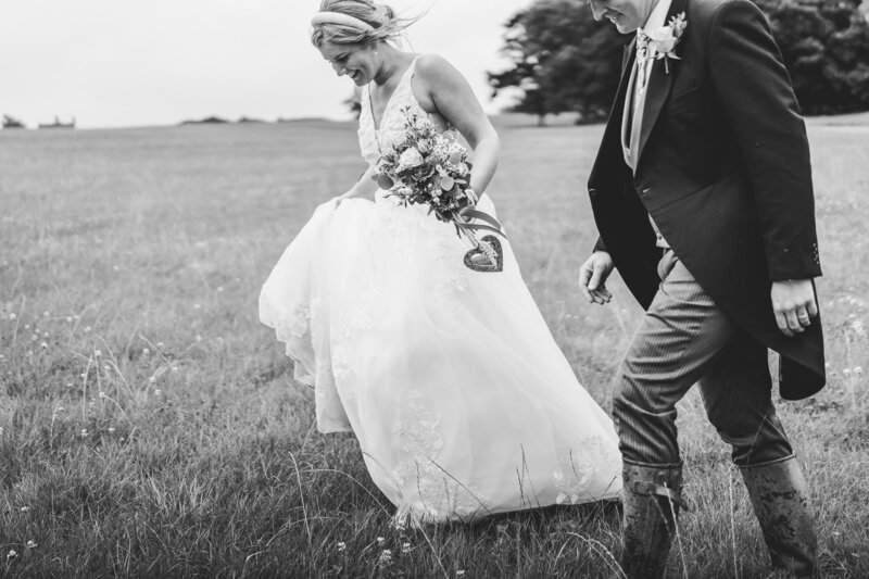 black and white image of wedding couple walking through field