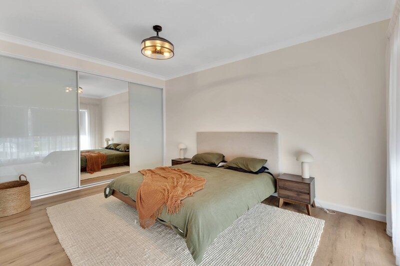 Contemporary bedroom featuring a queen bed with green linen, mirrored built-in wardrobe, bedside tables, and soft neutral styling for real estate photoshoot