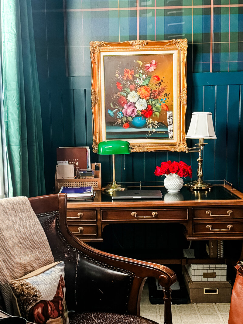 Plaid tartan wallpaper, blue wainscoting, green velvet curtains, floral oil painting, antique desk, brass lamp, green bankers lamp, milk glass vase with red roses. My workspace inspired by the English Countryside and Ralph Lauren. 