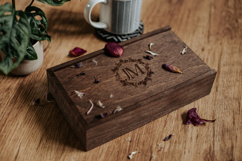 A dark wooden box with JM engraved on the front, surrounded by petals