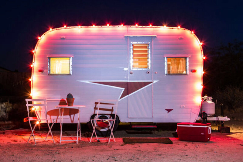 Branding Image Gatos Trail Studio trailer at night decorated with lights with a table two chairs and a cooler outside in front of it