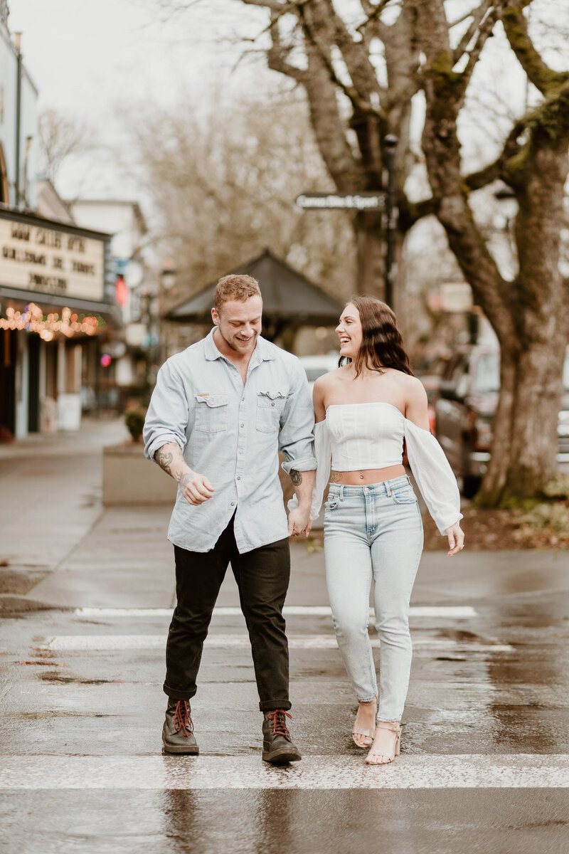 A happy engaged couple laugh and walk downtown holding hands