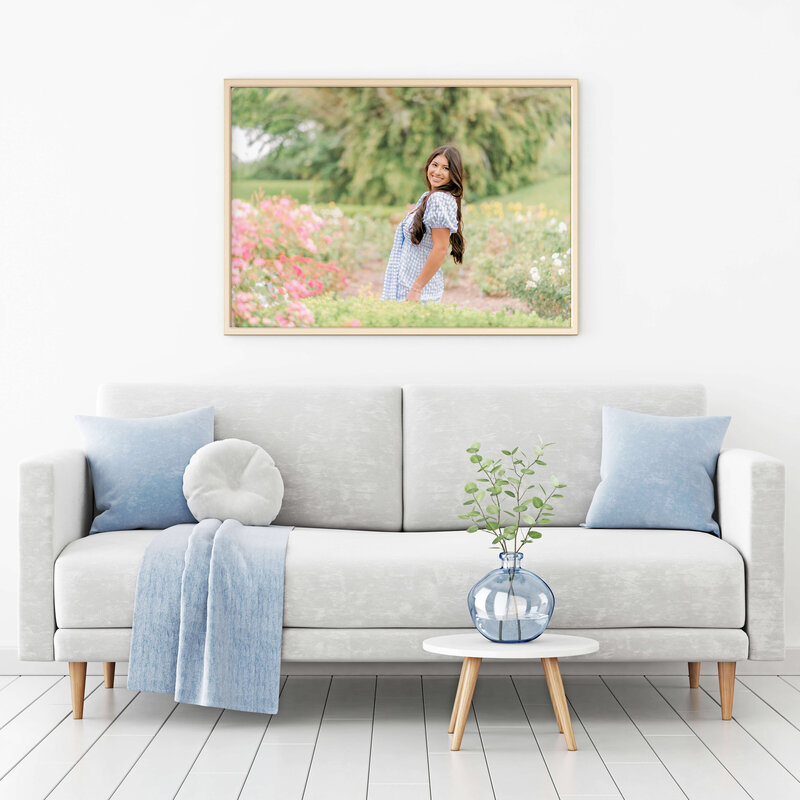 A gold framed portrait in a beautifully styled living room of a senior in a field of flowers.