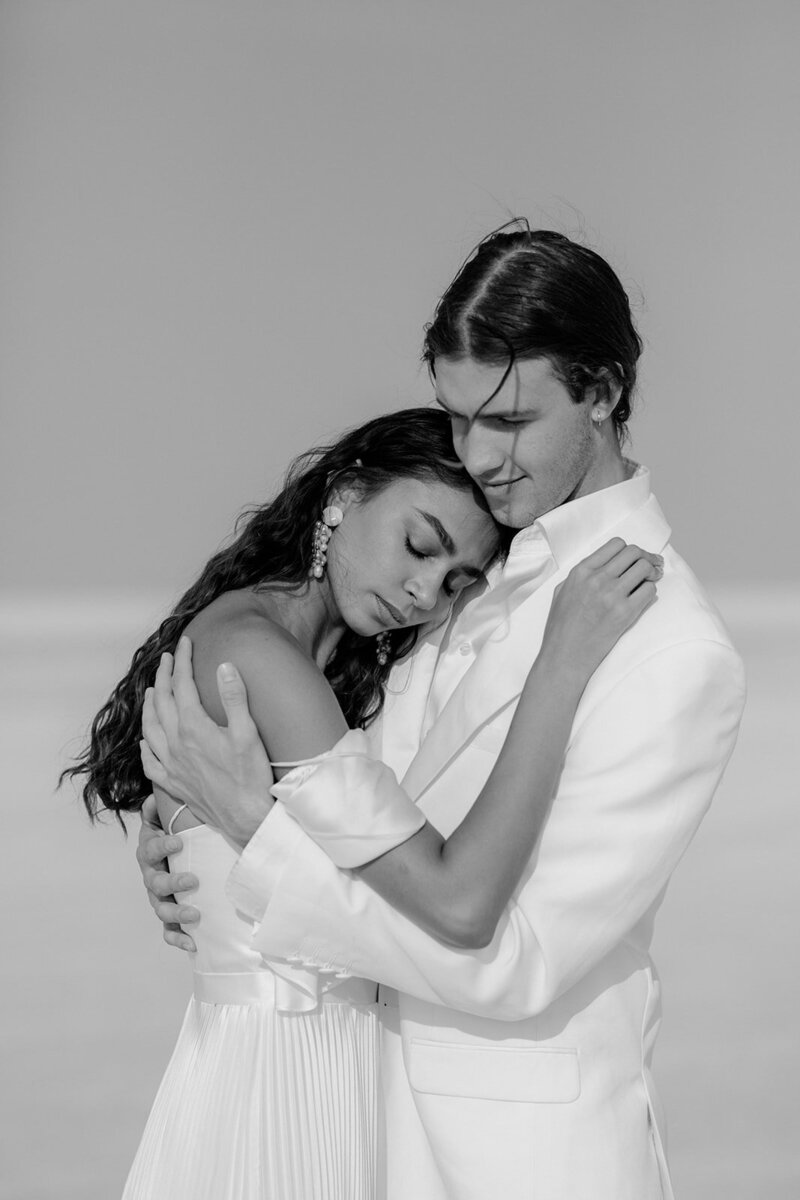 A couple embracing, the man in white and the woman in a pleated dress.