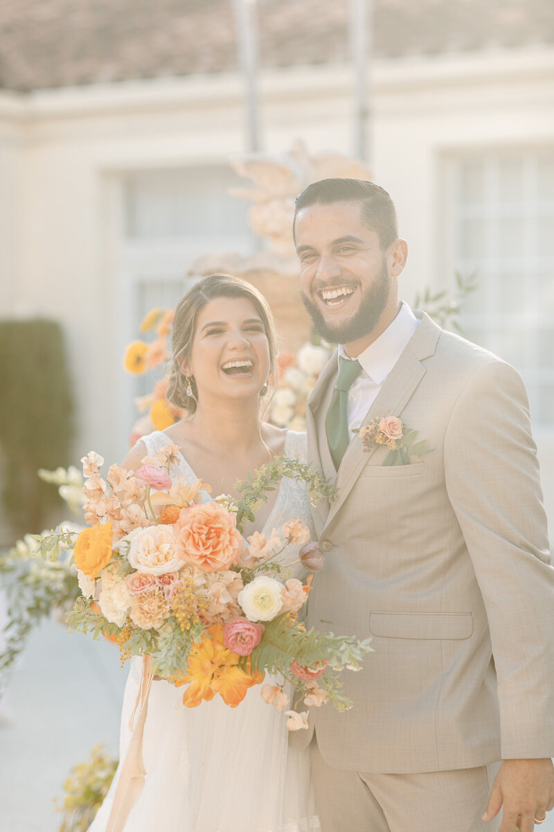 Bride and groom smile brightly while holding multi-colored bouquet