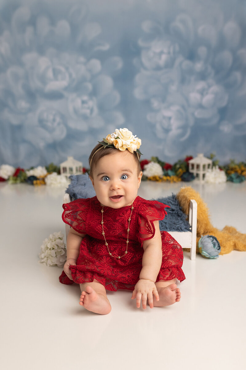 baby sitting in red dress with blue eyes by Philadelphia Newborn Photographer
