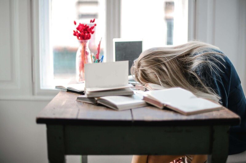 Sad student with their face on their books at their desks
