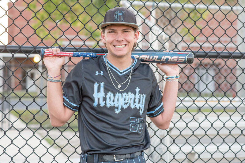 Hagerty high school baseball player photo session leaning on a fence at school.