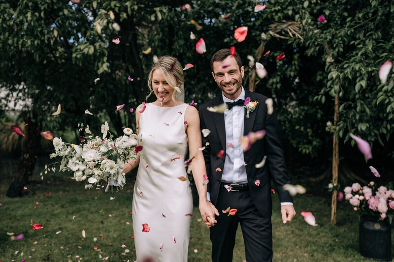 wedding guests throw red pink and white rose petals on newly married couples as confetti from mrs bottomleys